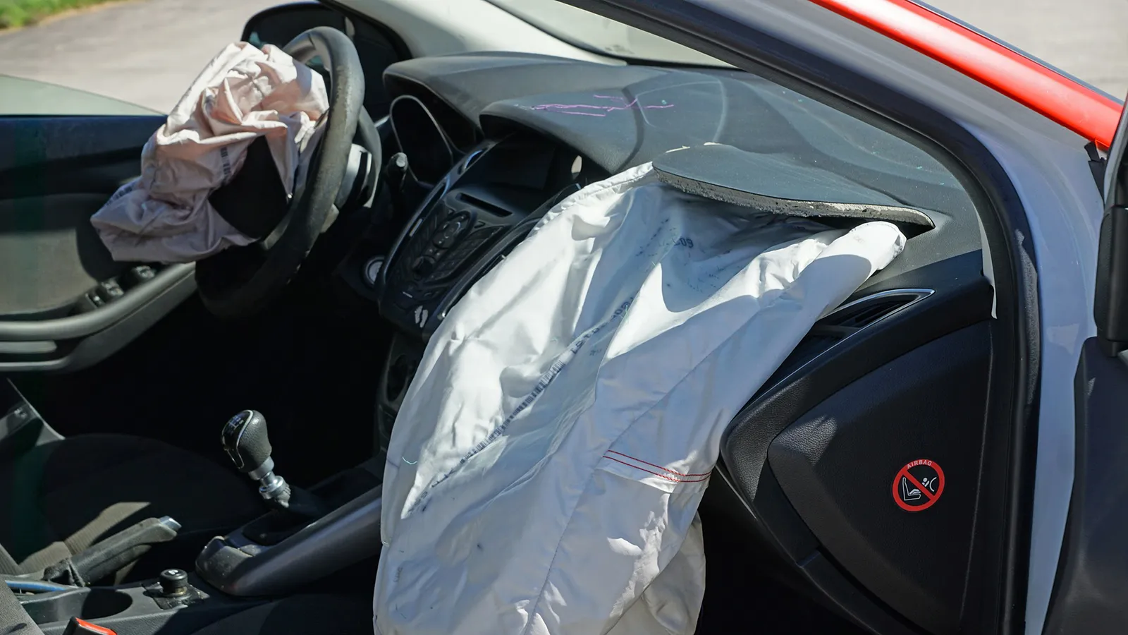 Interior of a crashed car with the driver and passenger airbags deployed across the steering wheel and dashboard