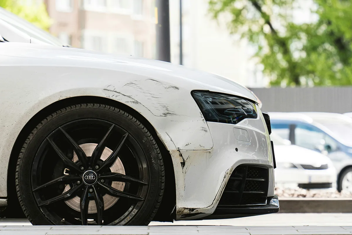 A white Audi coupe with a scraped, scuffed front bumper parked kerbside, an example of light cosmetic damage
