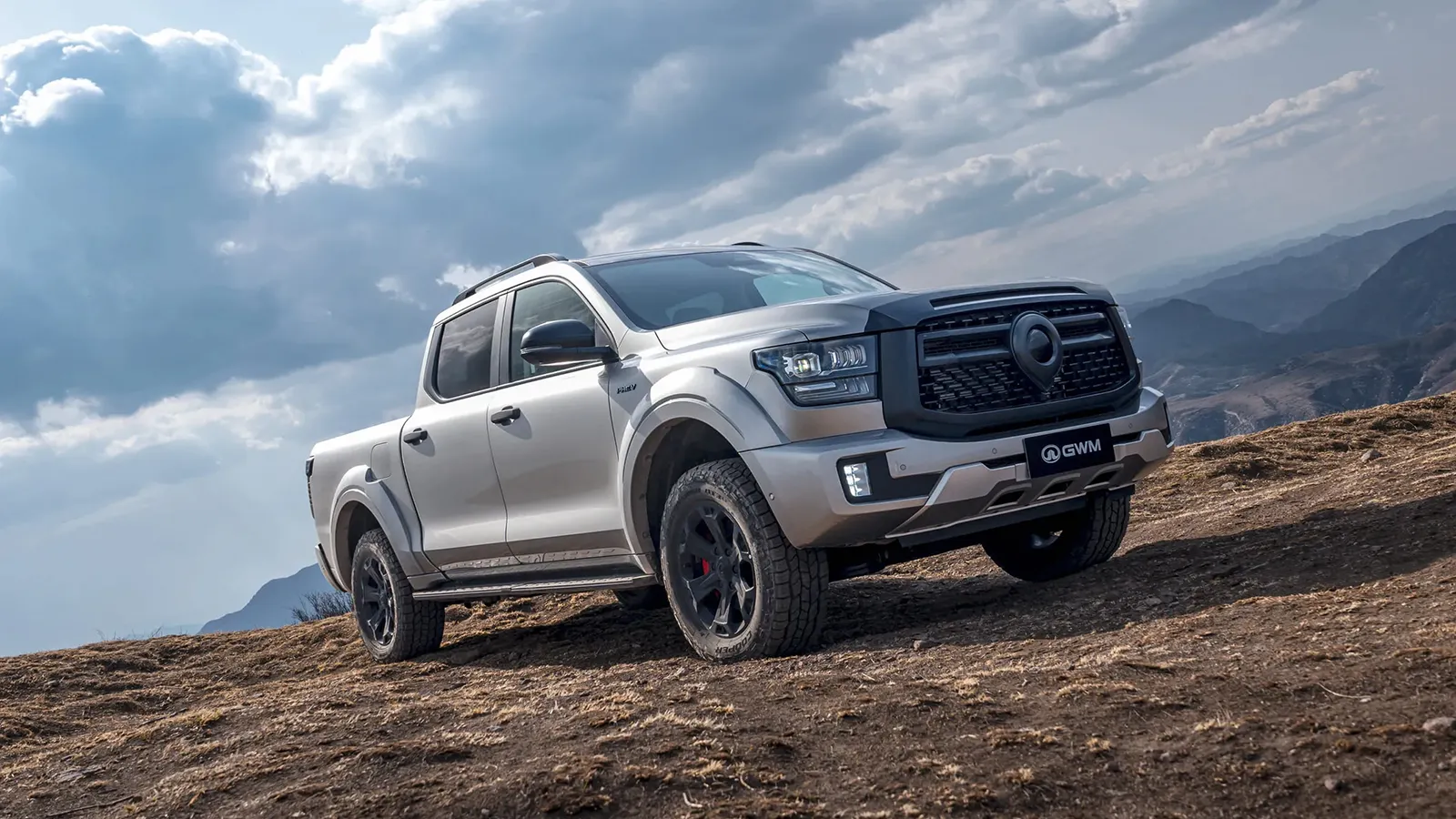 Silver GWM Cannon Alpha PHEV ute on a bare hilltop under stormy cloud, front three-quarter view with off-road tyres