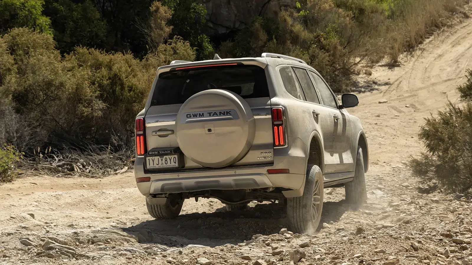 GWM Tank 500 HEV driving away on a dusty Australian off-road track, rear view