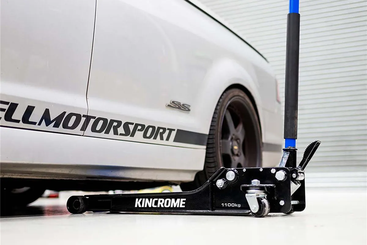 Kincrome K12164 1100kg super low-profile garage jack positioned under the rocker sill of a lowered sports car, workshop