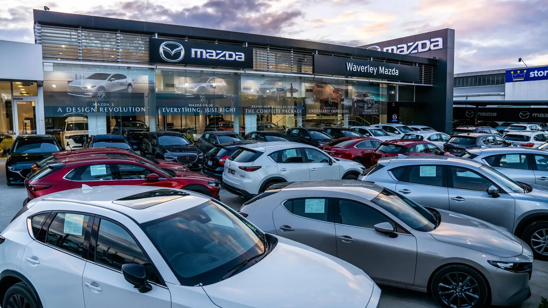 mazda-dealership-melbourne Waverley Mazda dealership forecourt with new cars on display at dusk, Melbourne