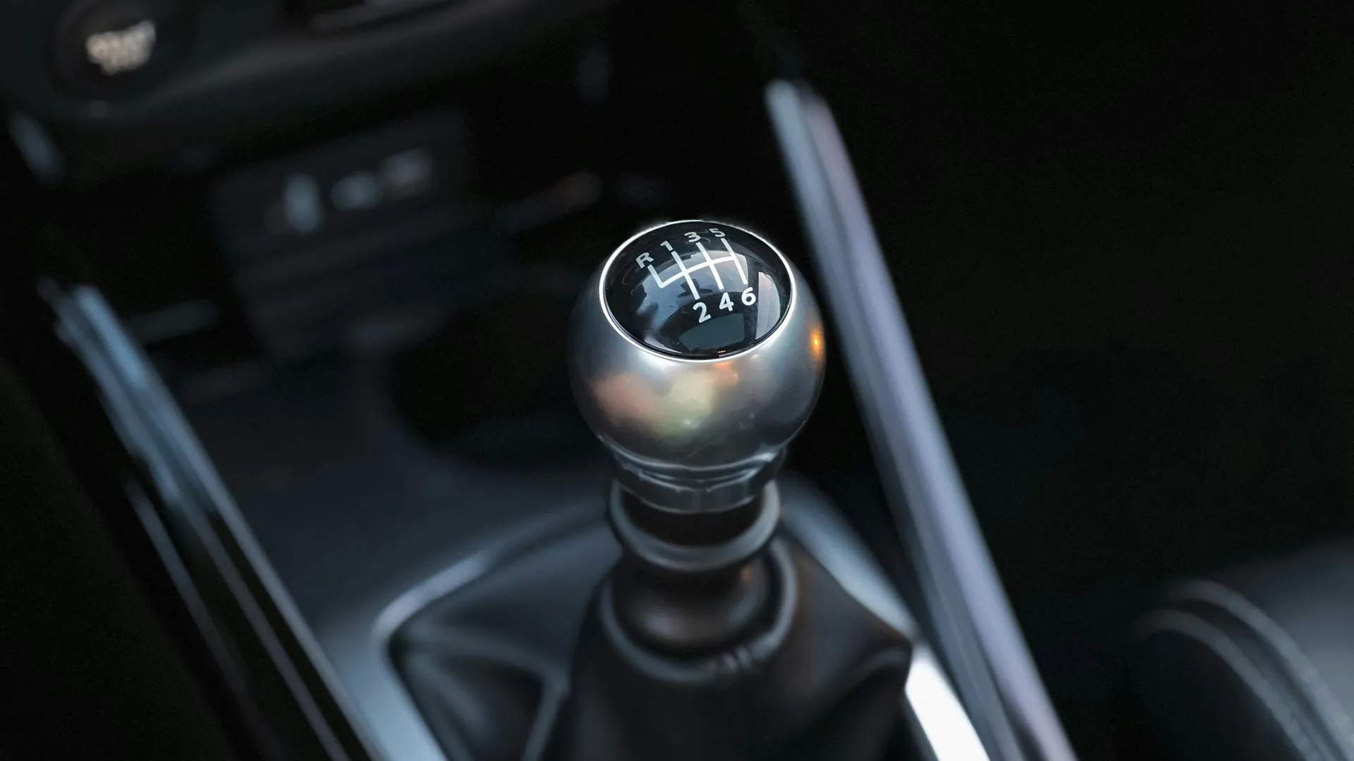 Close-up of a six-speed manual gear shifter with chrome knob and shift pattern engraved on top in a modern sports car