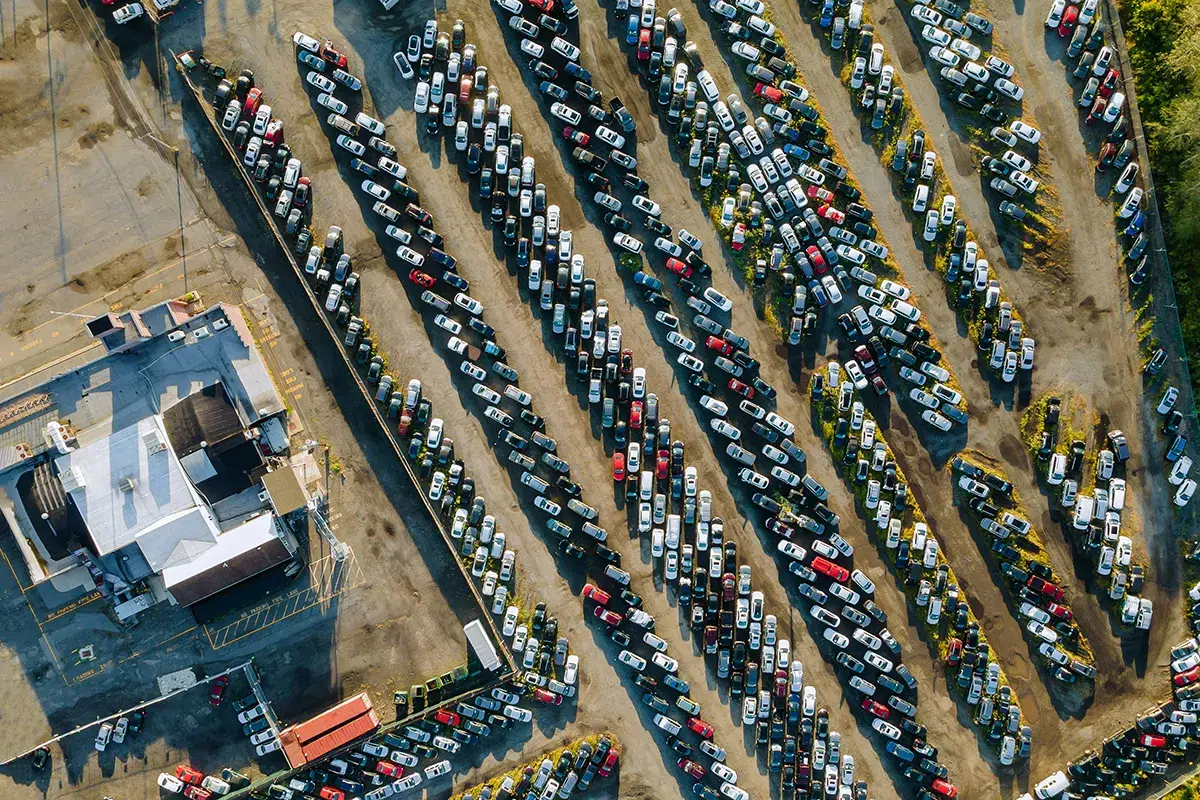 Aerial view of a salvage auction lot packed with rows of damaged and written-off cars beside a yard building