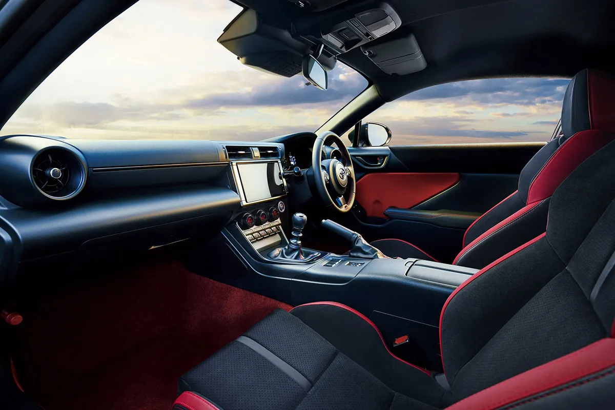 Right-hand-drive Toyota GR86 interior with red and black seats, manual gear lever and touchscreen