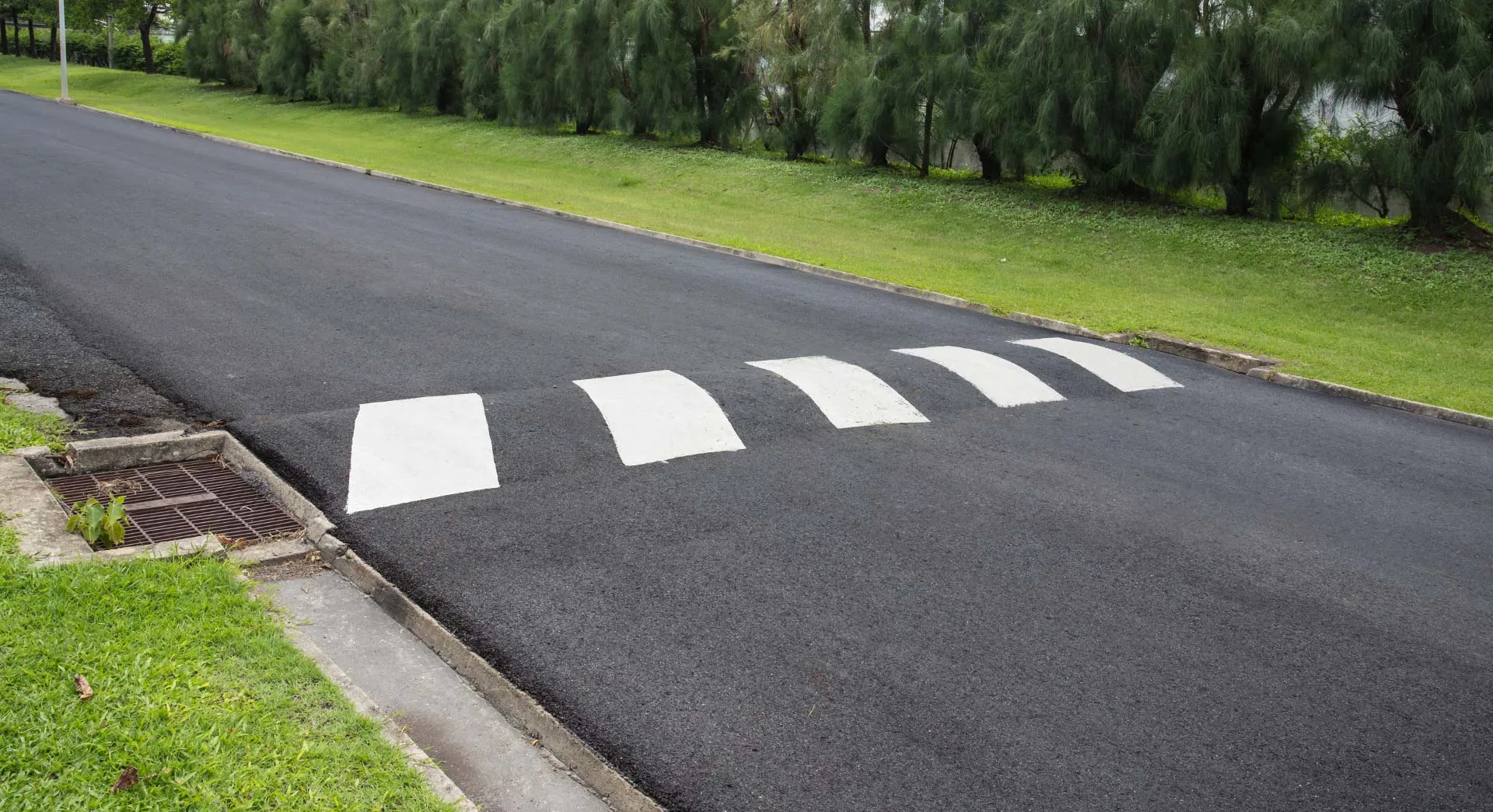 Asphalt speed hump with white piano-key markings across a suburban Australian street, tapering to the kerb beside a stormwater grate