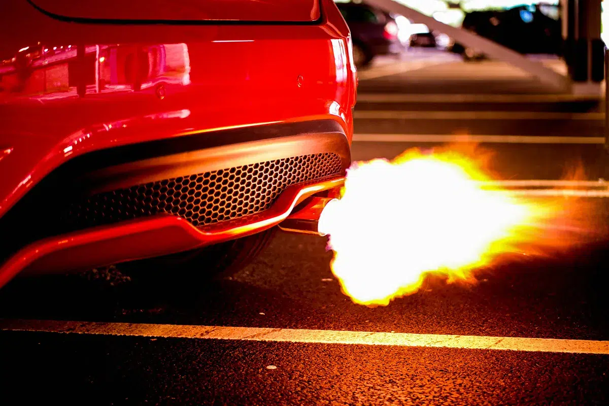 Flame shooting from the exhaust of a red car at night in a car park