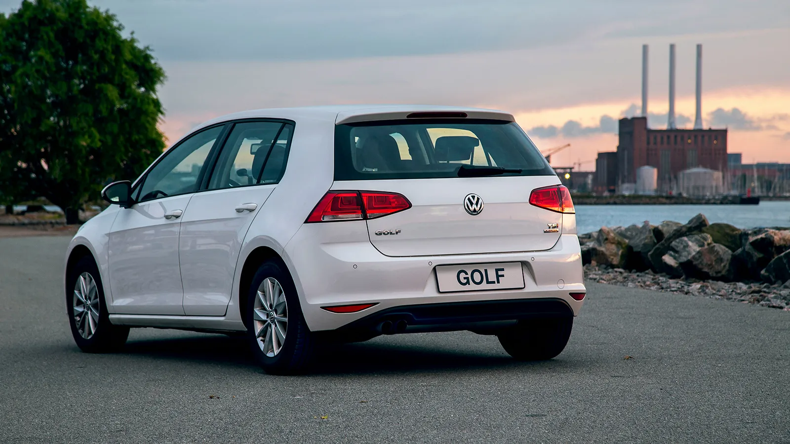 golf-mk7-tsi-docks White Volkswagen Golf Mk7 TSI rear three-quarter view parked on a waterfront with industrial towers behind