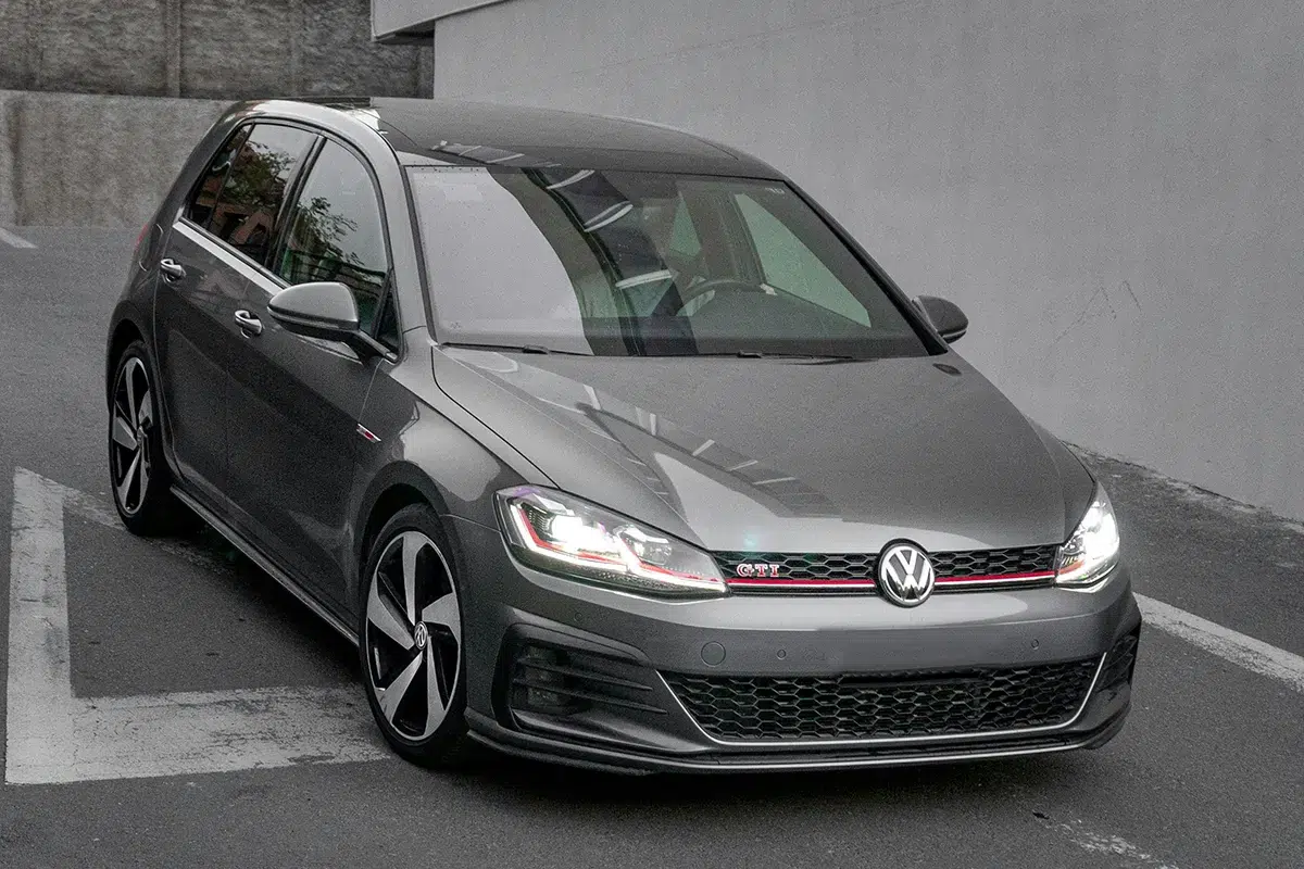 Dark grey Volkswagen Golf GTI Mk7.5 parked in a car park, front three-quarter view with headlights on