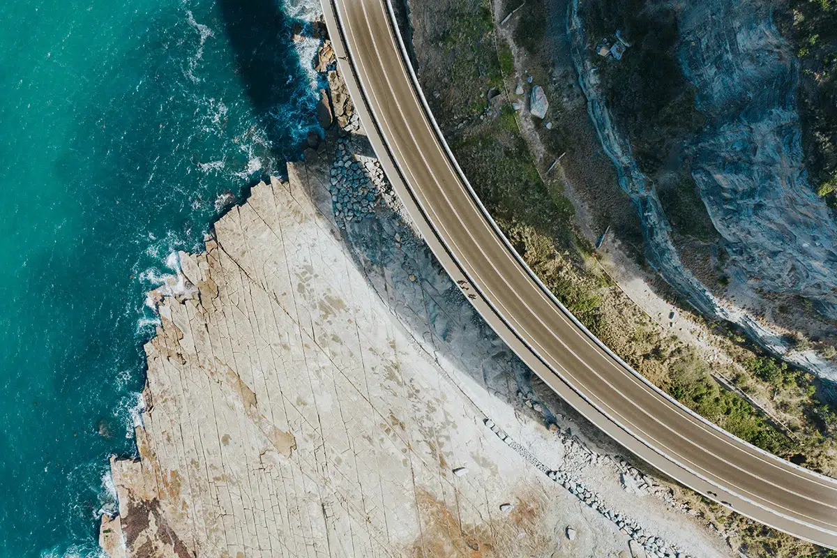 Aerial view looking straight down at a coastal road curving around a rock shelf above turquoise water