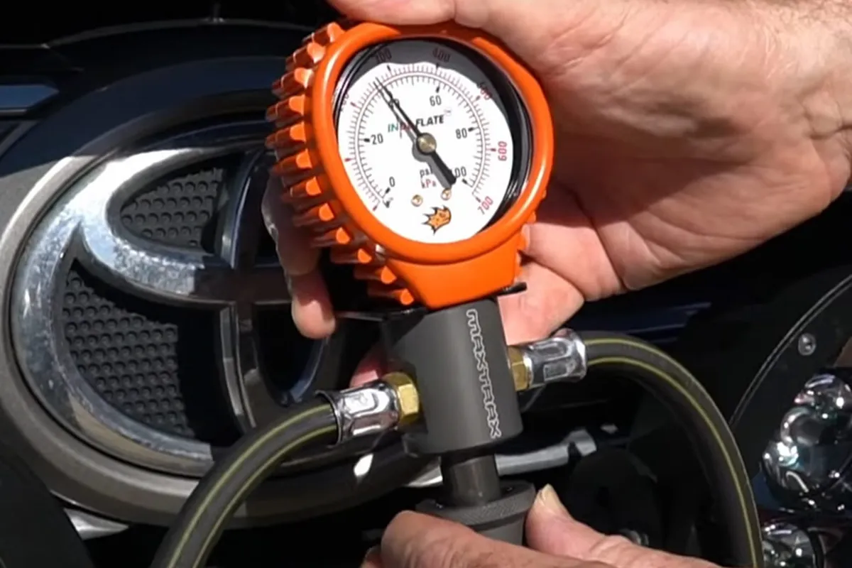 Hand holding an orange MAXTRAX Indeflate gauge with two air hoses connected, reading psi and kPa