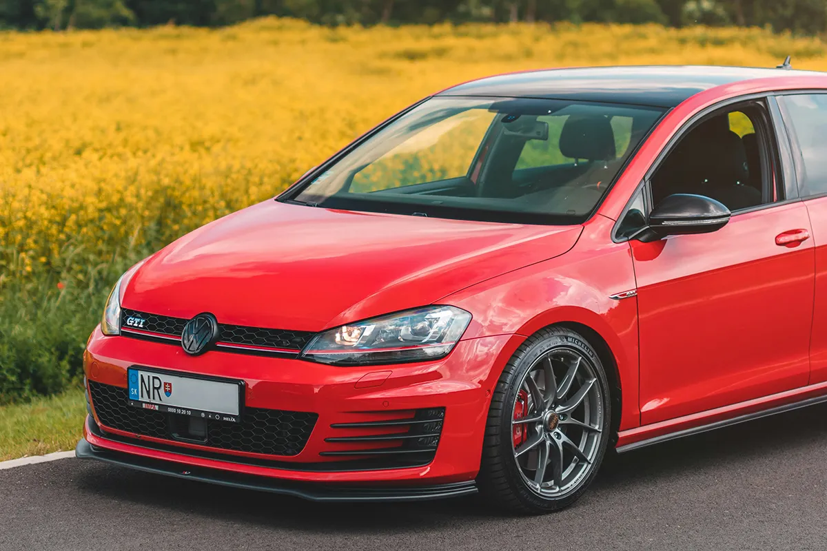Red Volkswagen Golf GTI Mk7 with aftermarket wheels and red brake calipers parked beside a canola field