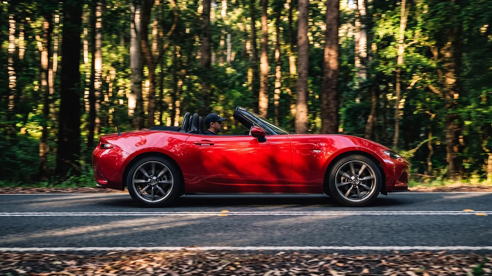 Red Mazda MX-5 travelling through forest on a two-lane road, side profile with motion blur