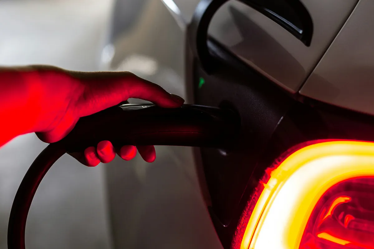 Hand plugging a charging cable into an electric car with the red tail light glowing