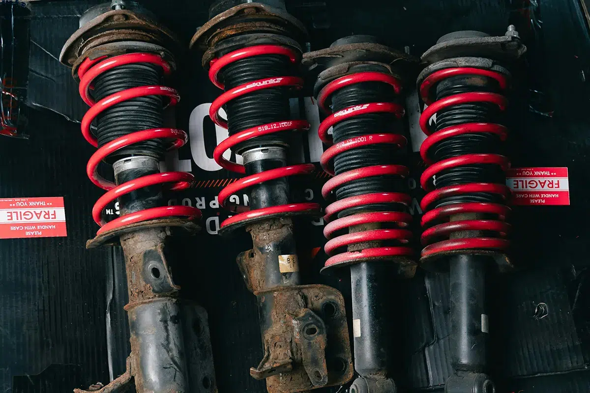 Four used strut assemblies with red aftermarket lowering springs fitted, showing heavy rust and wear