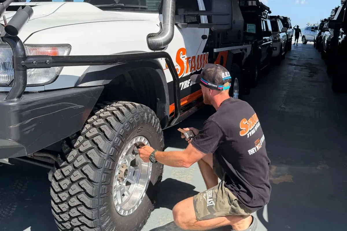 staun-tyre-deflater-using Man in Staun-branded shirt crouched at the front wheel of a white four-wheel drive ute fitting deflators