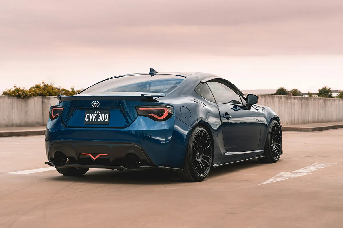 toyota-86-aus-rooftop Blue Toyota 86 lowered on black alloy wheels, parked on a rooftop car park, rear three-quarter view