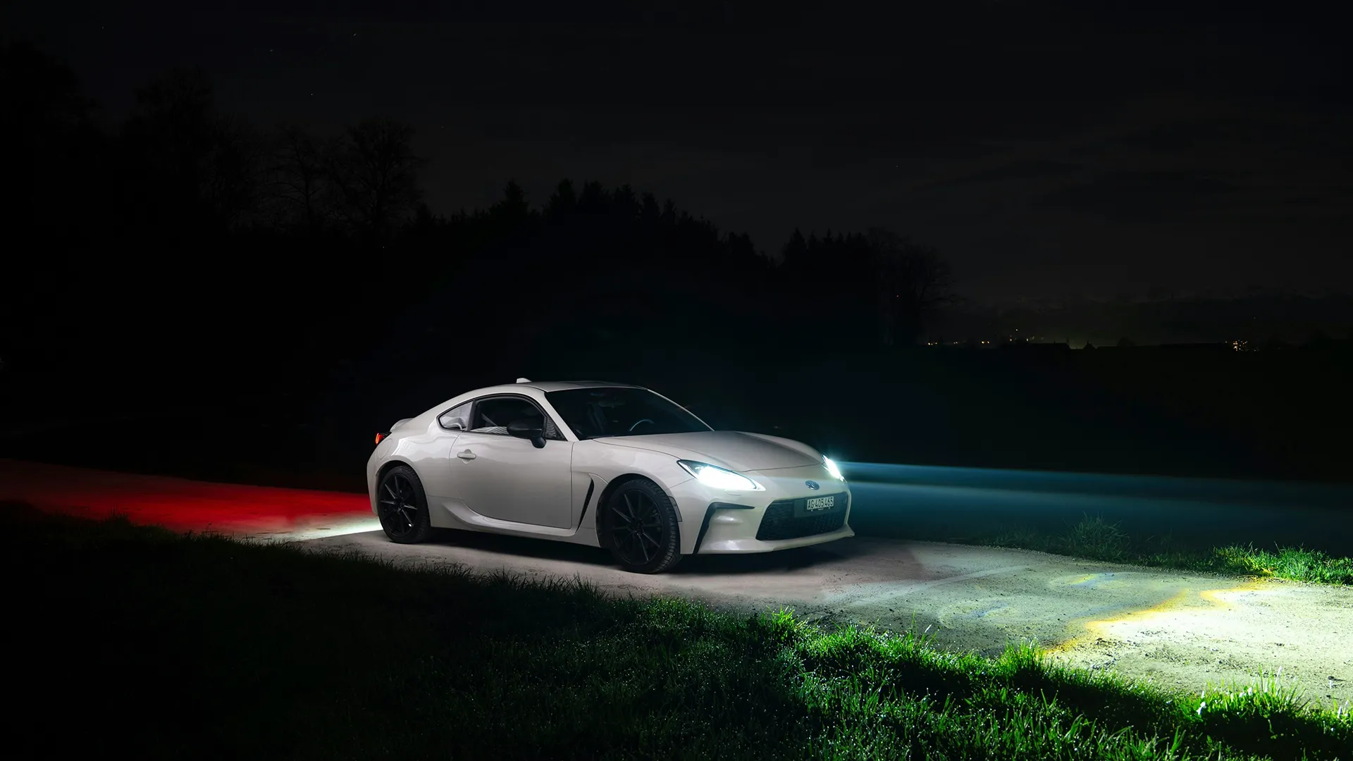 toyota-gr86-white-night White Toyota GR86 at night lit by red and white light painting on a rural road, front three-quarter