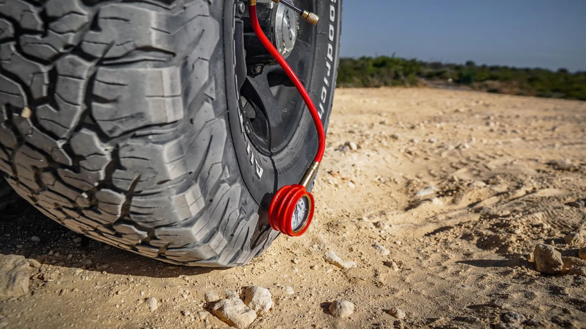 Coiled red hose and pressure gauge attached to a BFGoodrich four-wheel drive tyre on rocky ground