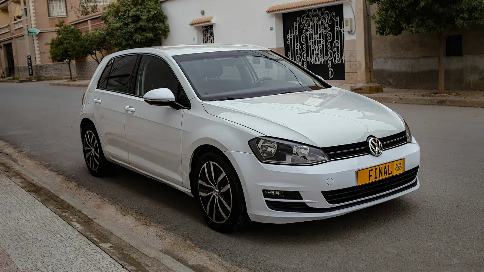 White pre-facelift Volkswagen Golf Mk7 parked on a suburban street, front three-quarter view