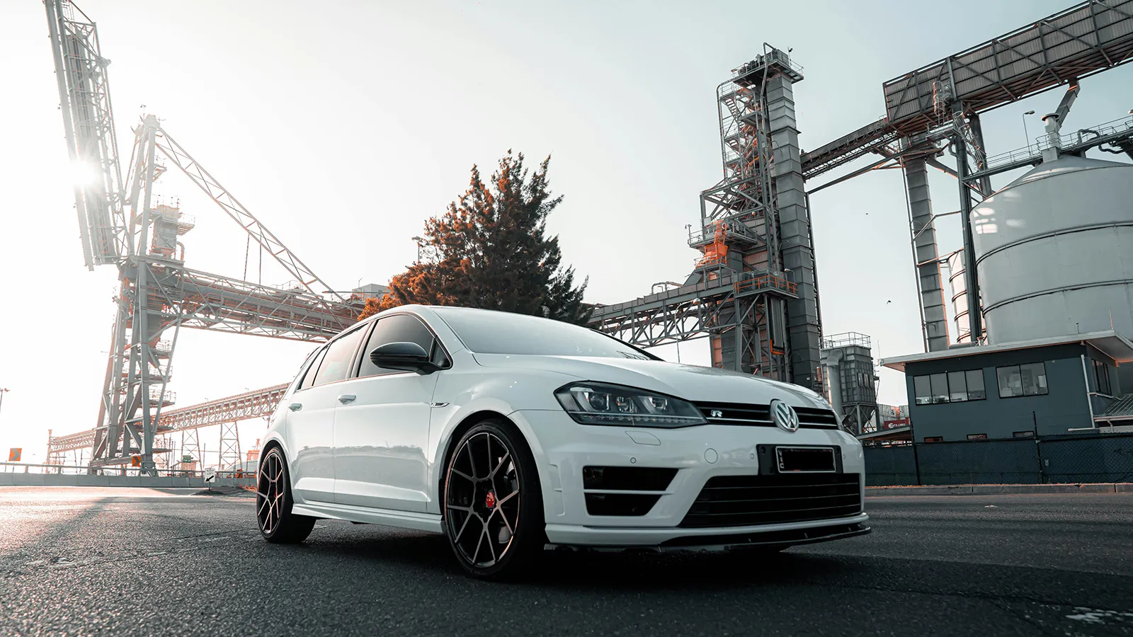 Modified white Volkswagen Golf R Mk7 on black wheels with red brake calipers at an industrial site