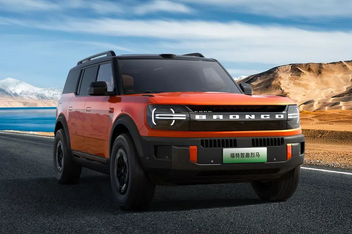 Chinese-market Ford Bronco in orange with a black roof, front three-quarter view on a desert highway