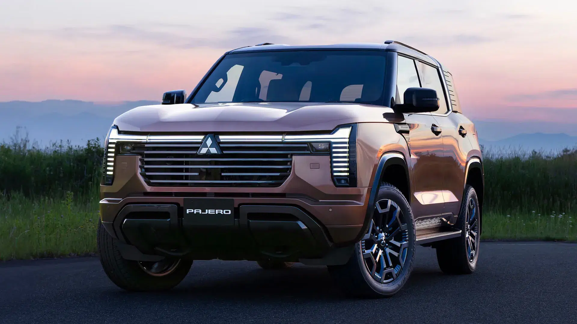 New Mitsubishi Pajero front three-quarter view parked roadside at dusk with mountains in the background
