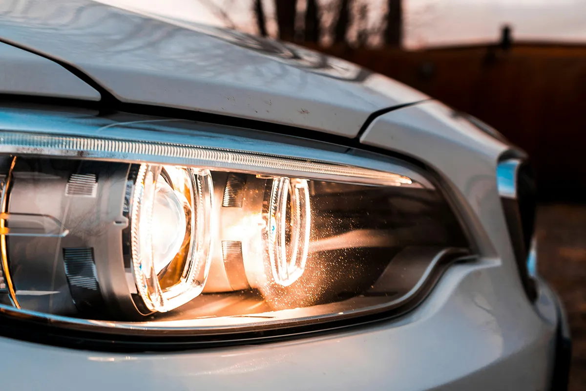 Close-up of an illuminated BMW headlight at dusk showing a clear polycarbonate lens