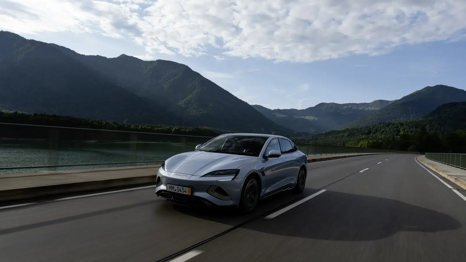 Grey BYD Seal electric sedan driving on a lakeside road with mountains in the background