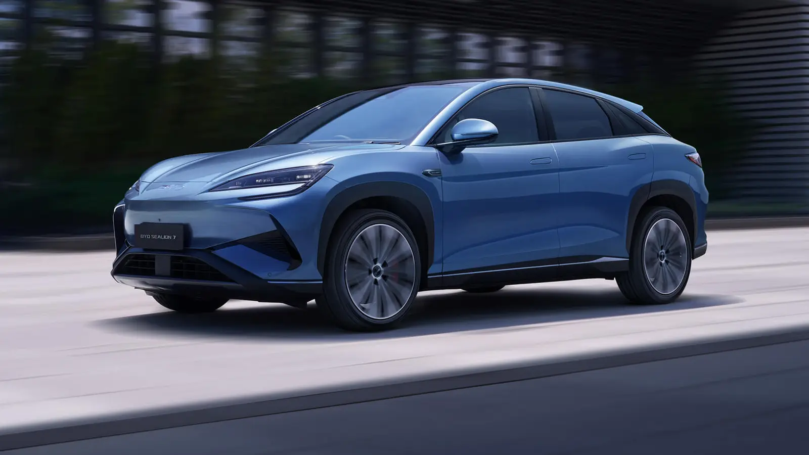 Blue BYD Sealion 7 electric SUV driving on a city road with motion blur behind it