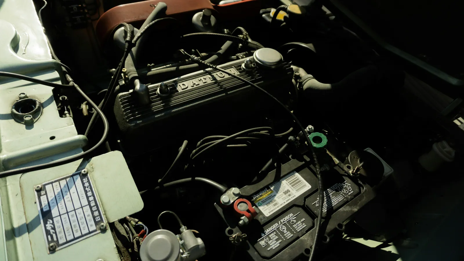 Conventional lead-acid car battery sitting in the engine bay of an older car, surrounded by wiring
