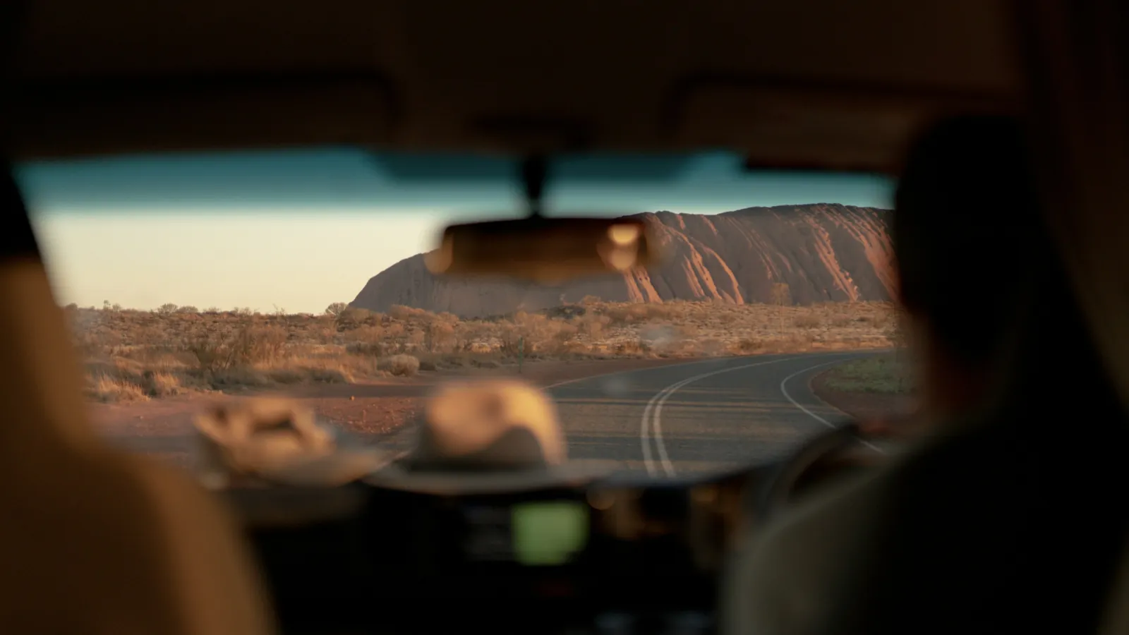 View through a car windscreen driving toward Uluru on a hot, dry outback road in the Northern Territory
