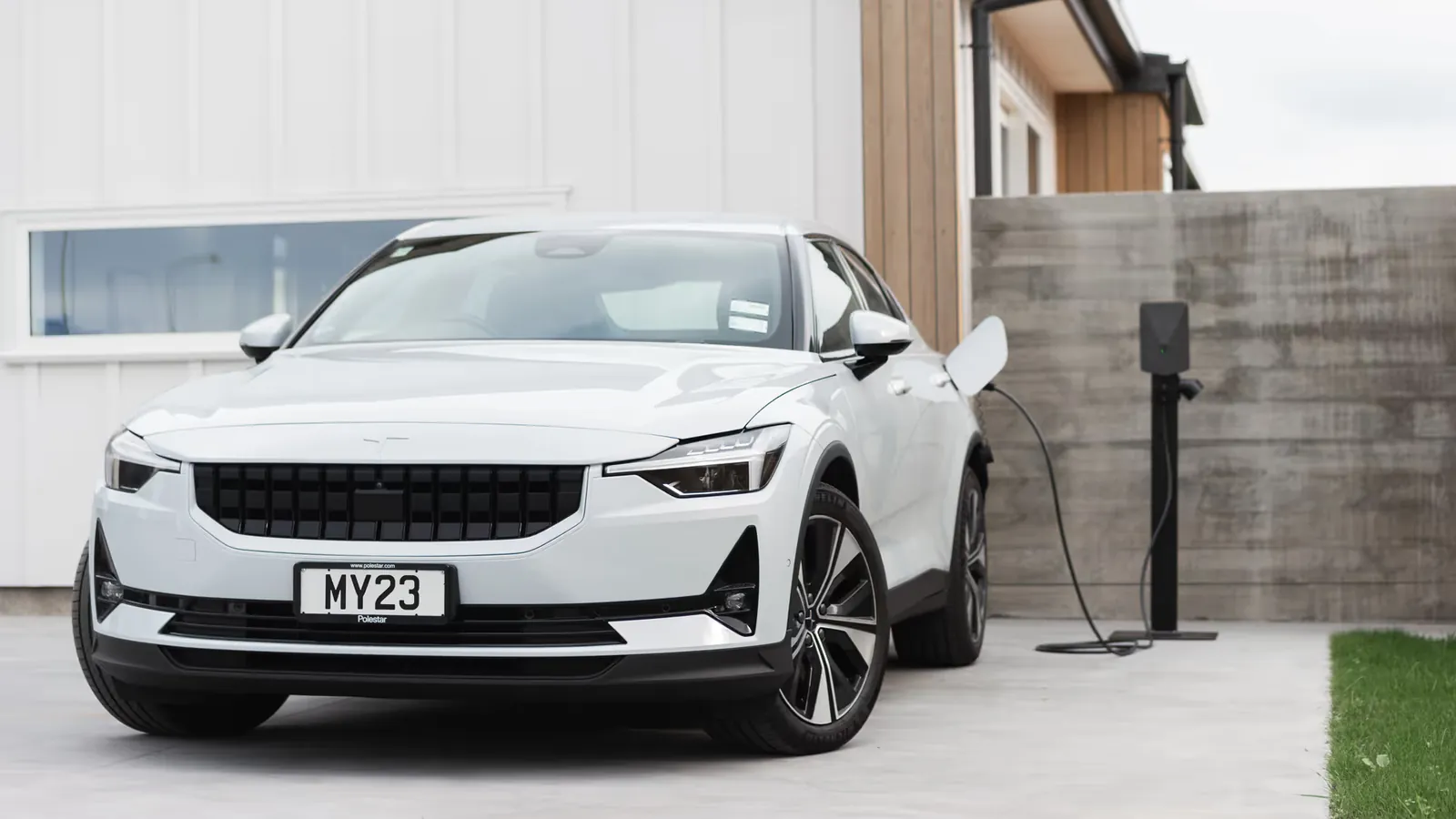White Polestar 2 plugged into a pedestal-mounted Evnex E2 home EV charger on a driveway