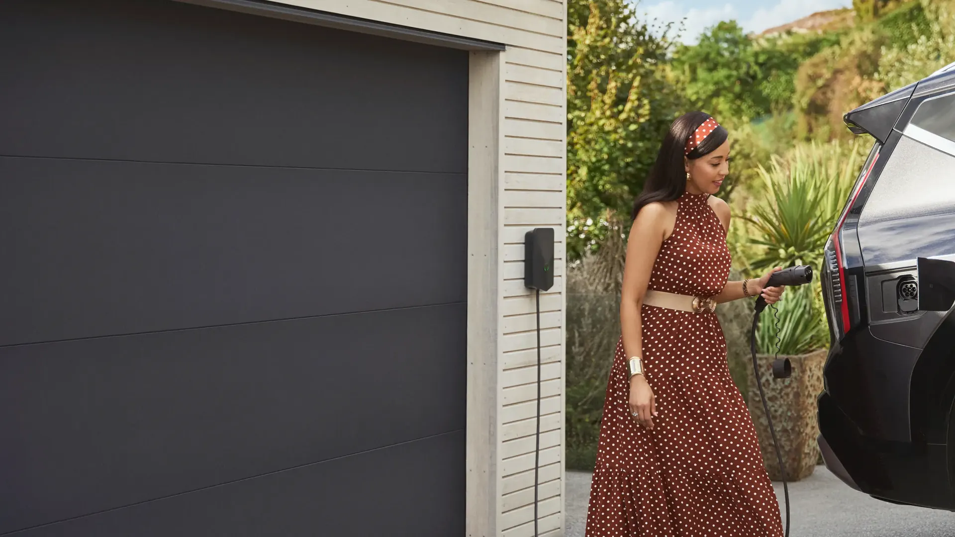 Home EV charger beside a garage Woman plugging an electric SUV into a wall-mounted home EV charger beside a garage door