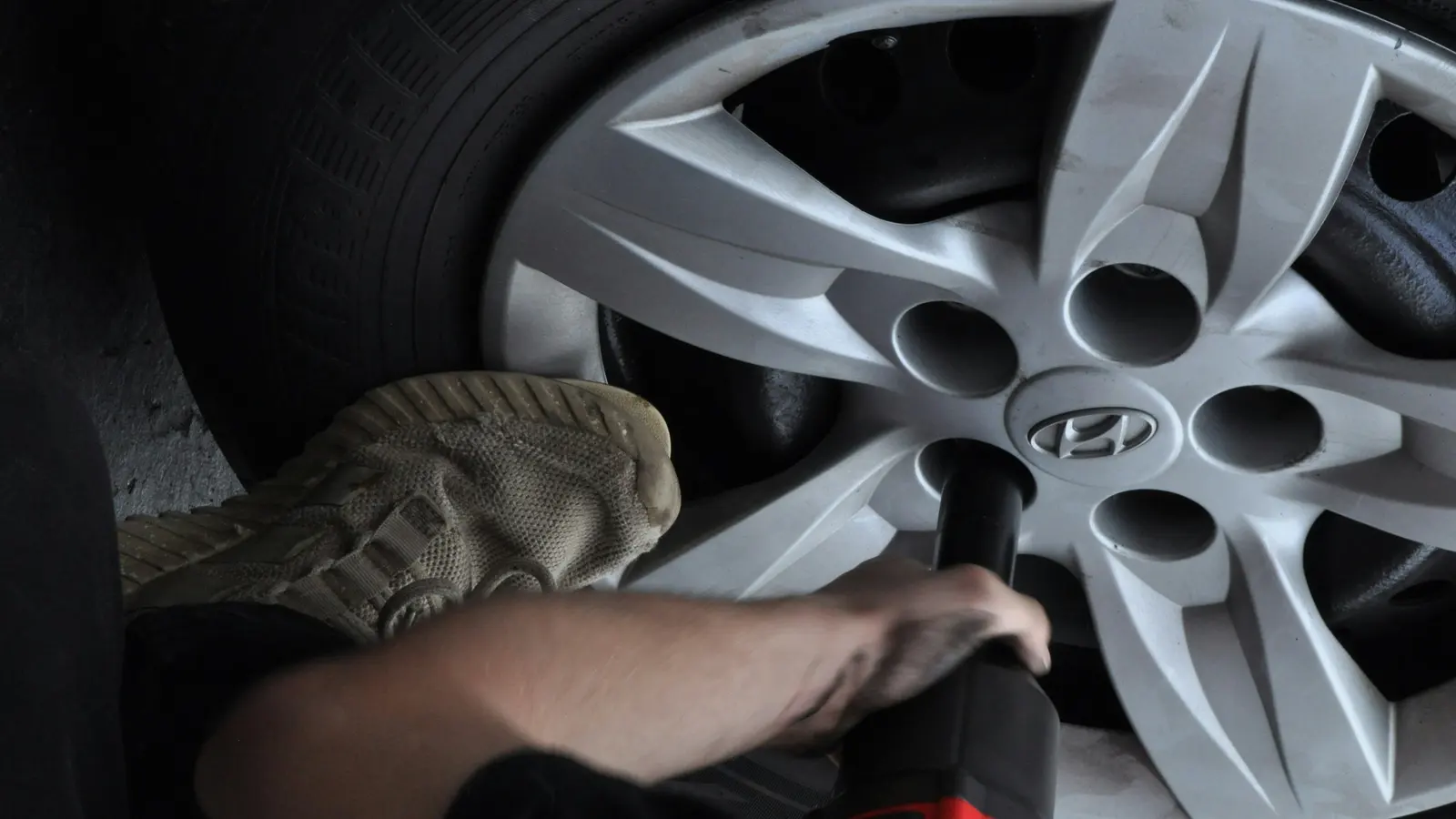 Mechanic using a cordless impact wrench on the wheel nuts of a silver alloy car wheel