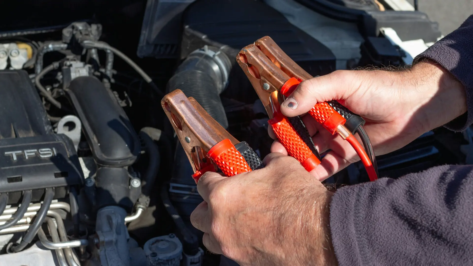 Jumper leads over a flat car battery Hands holding red jumper lead clamps over an open engine bay, ready to jump start a flat car battery