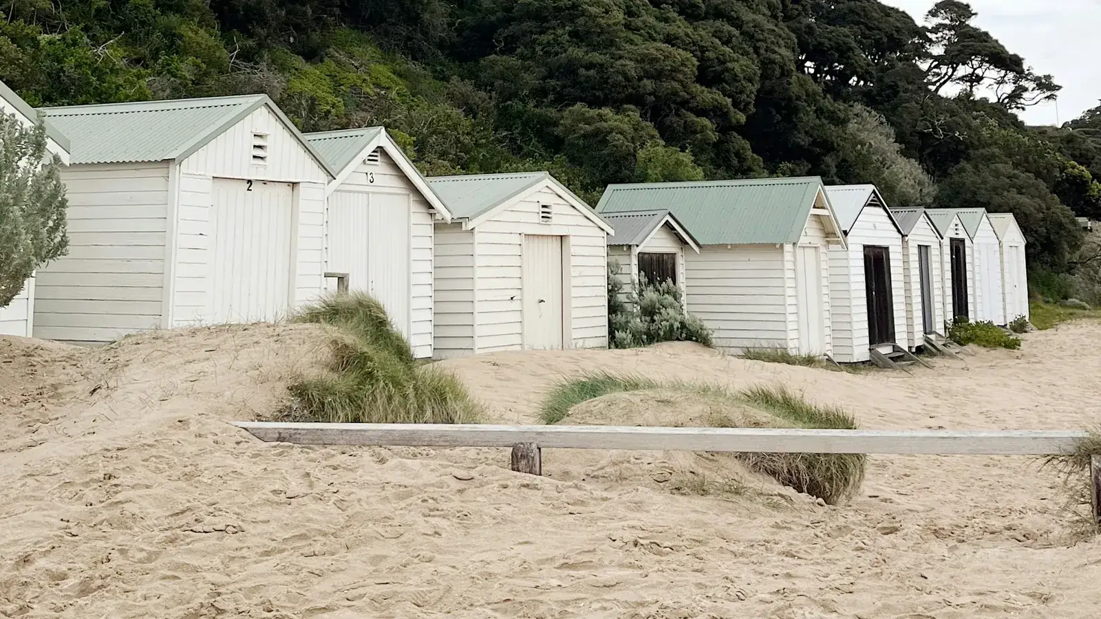 Row of white timber bathing boxes with green roofs on a sandy Mornington Peninsula beach