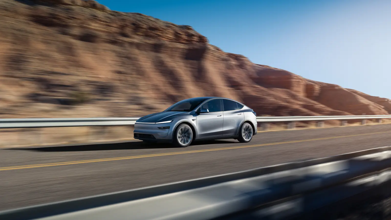 Silver 2026 Tesla Model Y Premium driving along an open desert highway past red rock cliffs