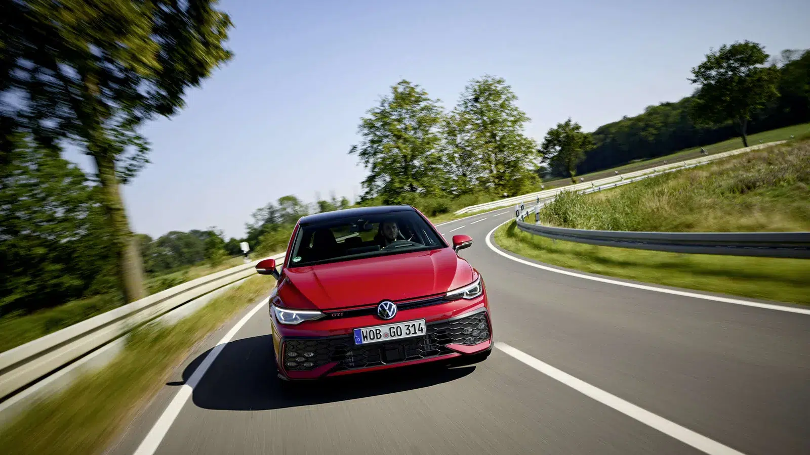 Red Volkswagen Golf GTI Mk8.5 hatchback driving along a winding country road, front view