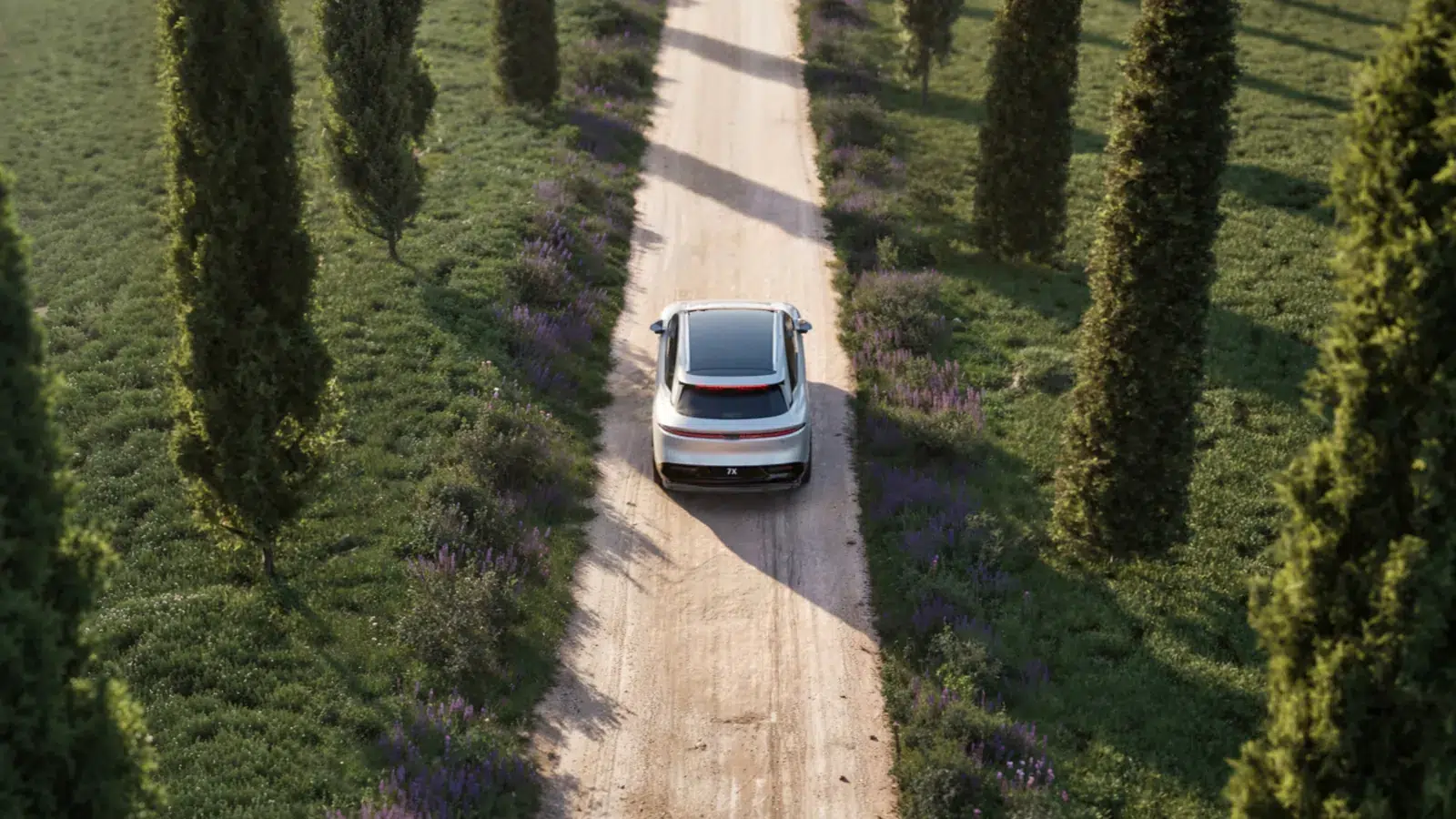 Aerial view of a white Zeekr 7X driving down a gravel road lined with cypress trees