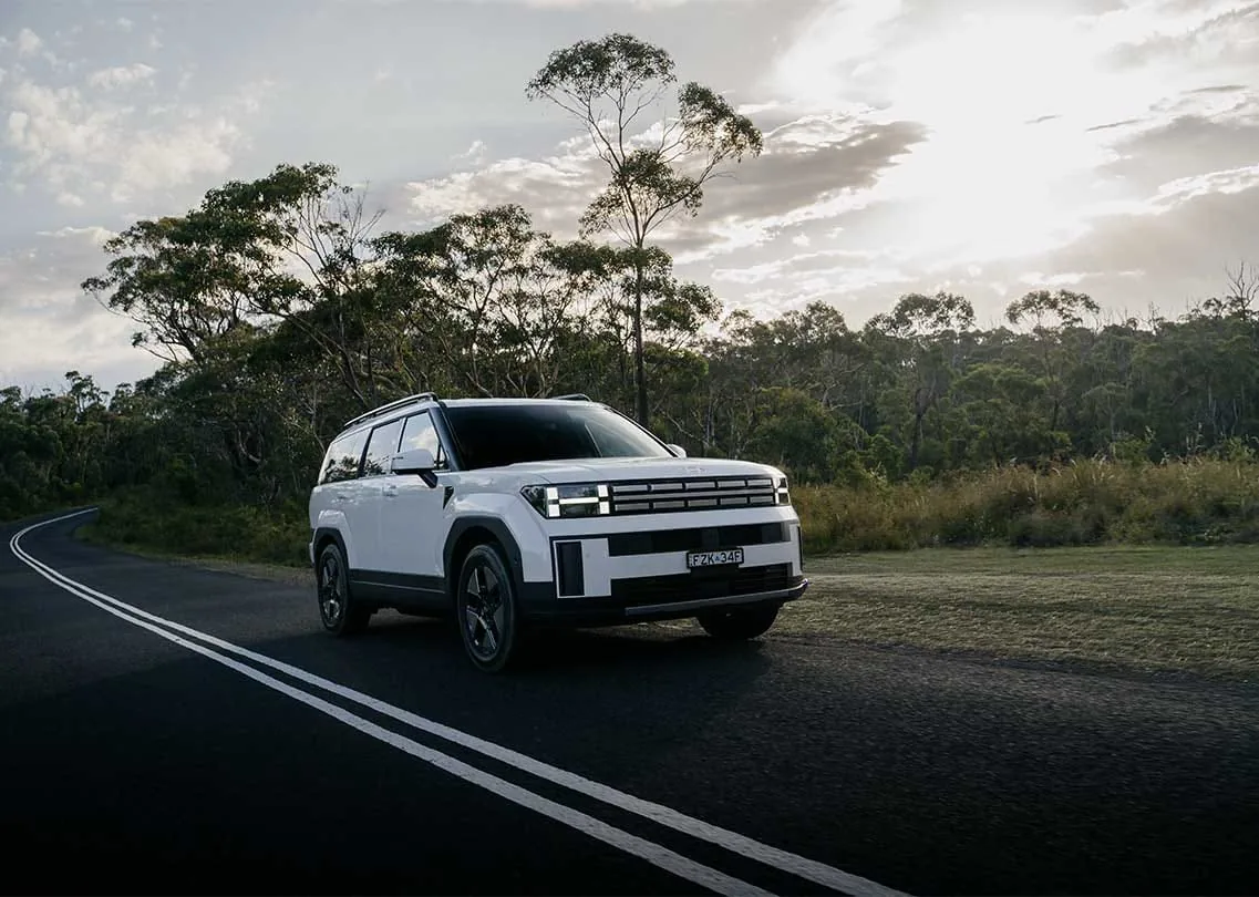 White 2026 Hyundai Santa Fe Hybrid on a winding road through Australian bush, front three-quarter view