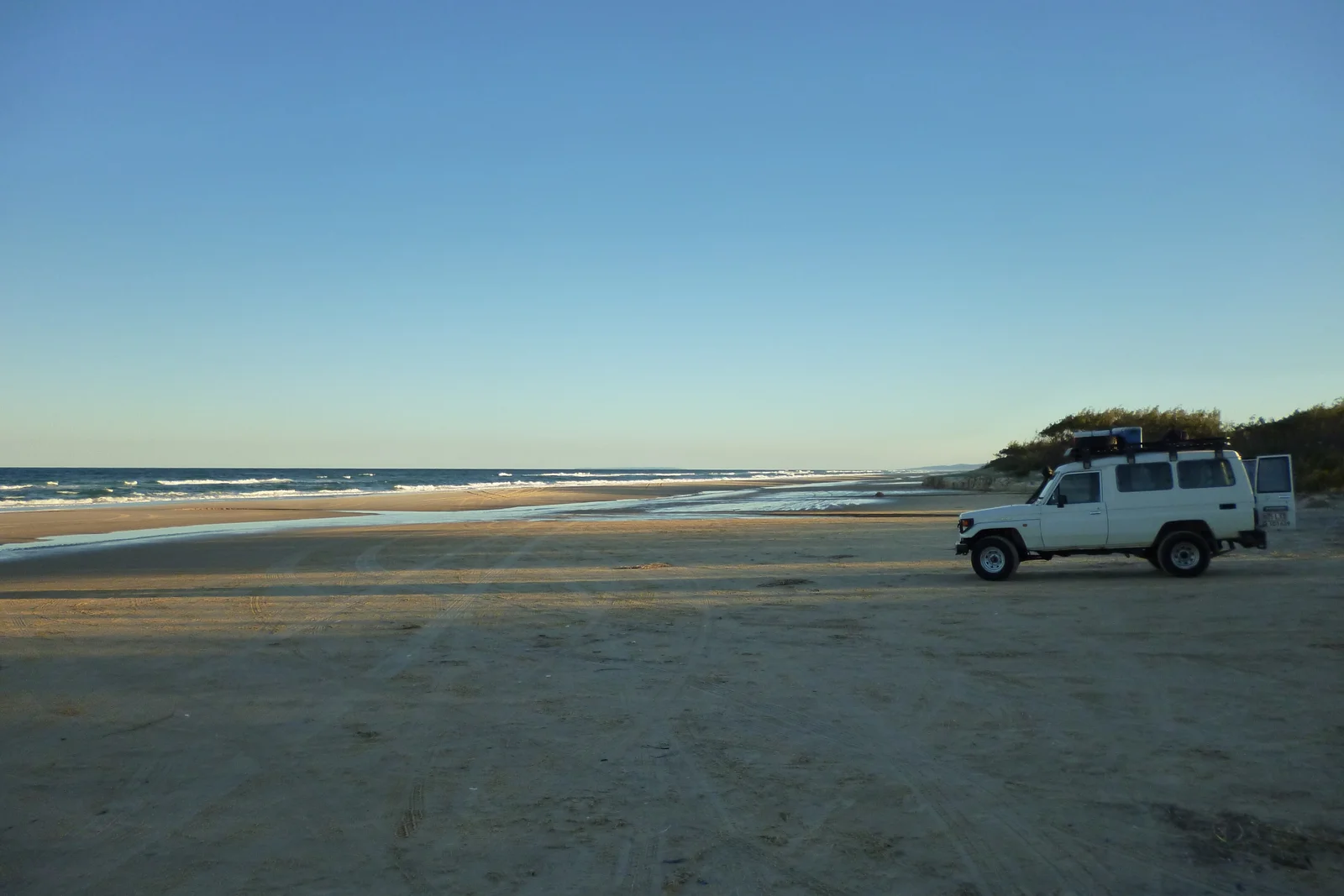 Toyota LandCruiser 70 Series Troopy parked on the hard sand of a K'gari (Fraser Island) beach at dusk
