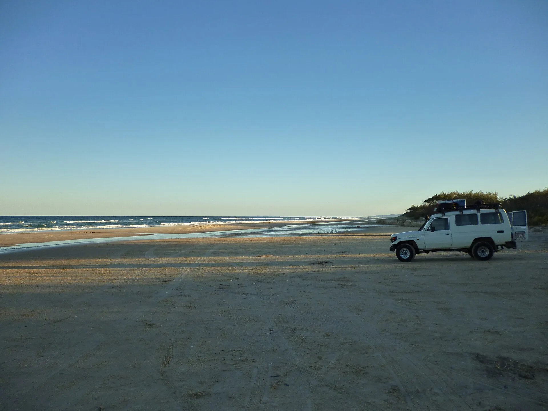 White Toyota LandCruiser 70 Series troop carrier parked on hard sand near the water on an Australian beach