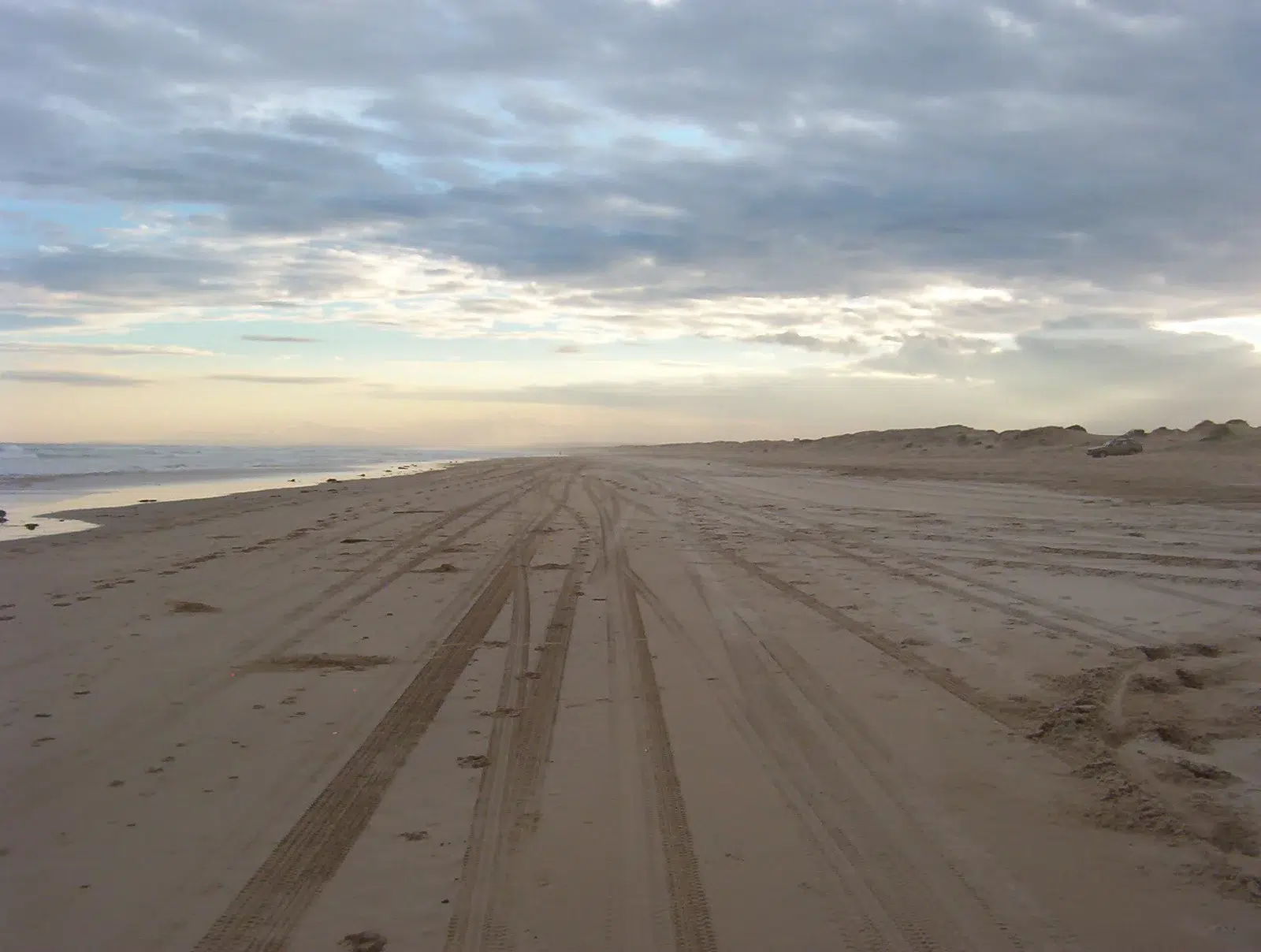Deep 4WD tyre tracks in soft sand on Stockton Beach, Port Stephens, under a cloudy sky