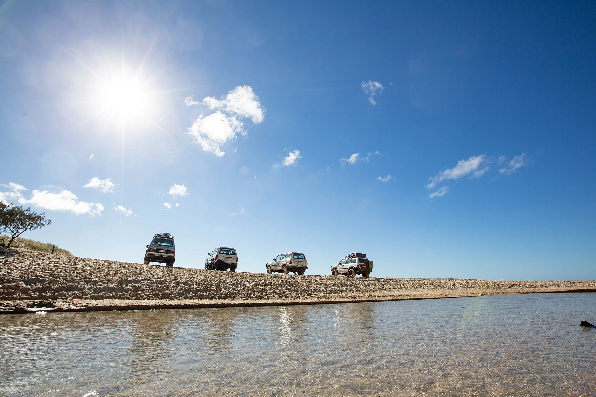 Four 4WDs parked on the beach beside the shallow, clear freshwater of Eli Creek on K'gari