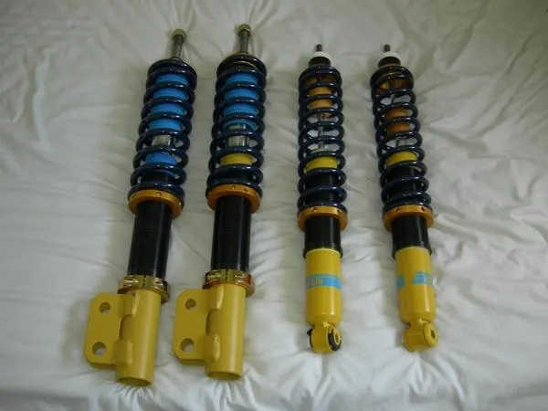 Set of four aftermarket coilovers with blue springs and yellow adjustable bodies laid out side by side