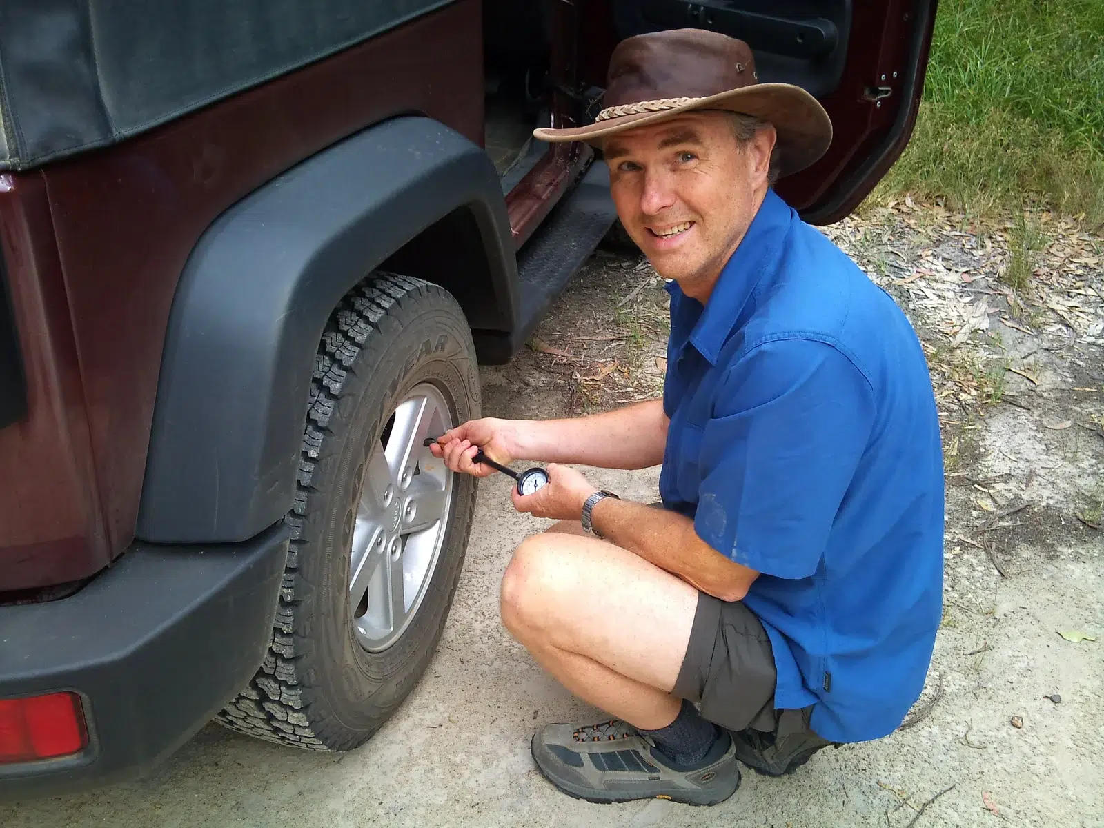Man crouching beside a 4WD to let air out of the tyre before an off-road drive near Lithgow, NSW