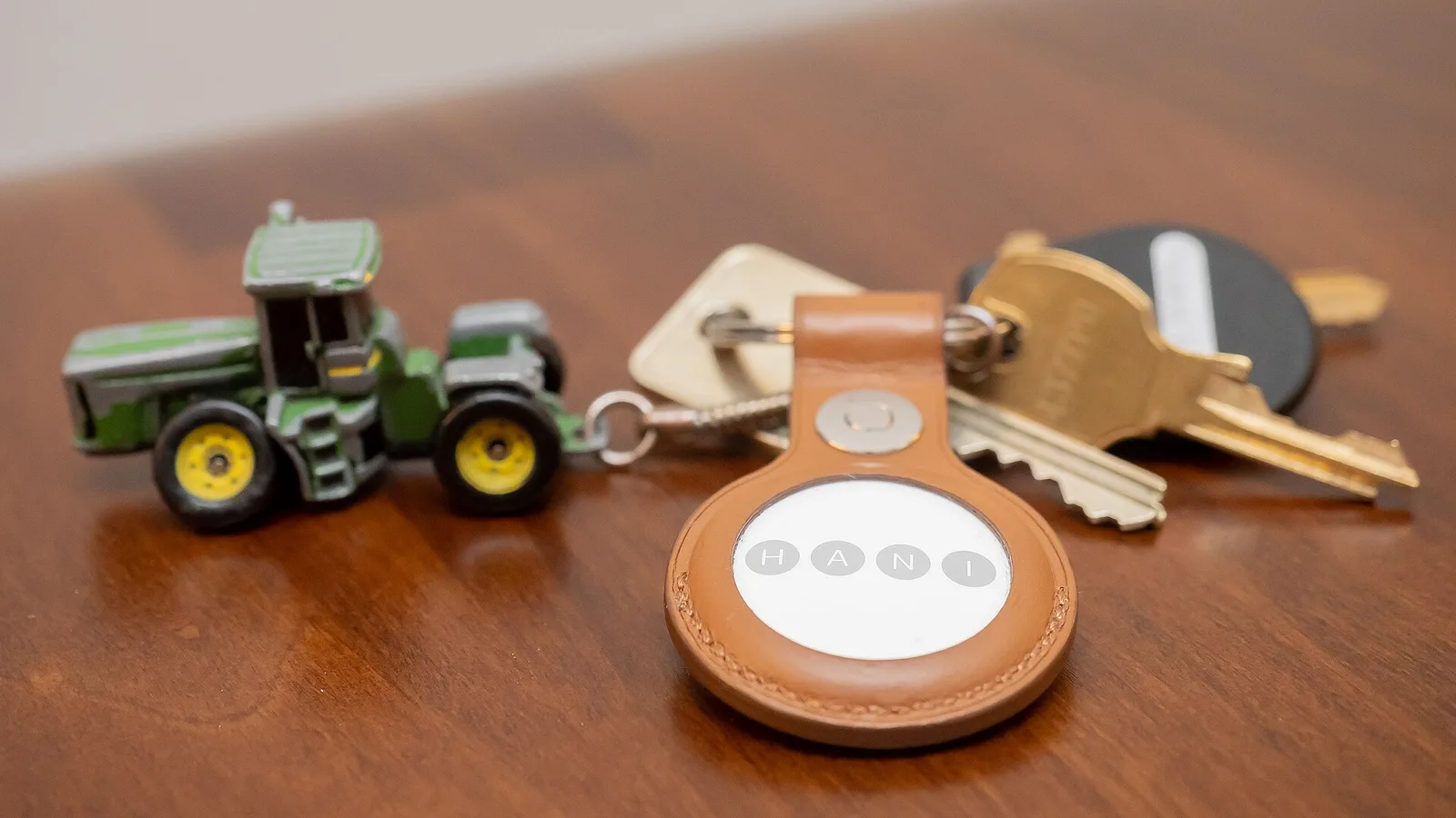 Apple AirTag in a tan leather key ring holder attached to a set of keys on a timber table