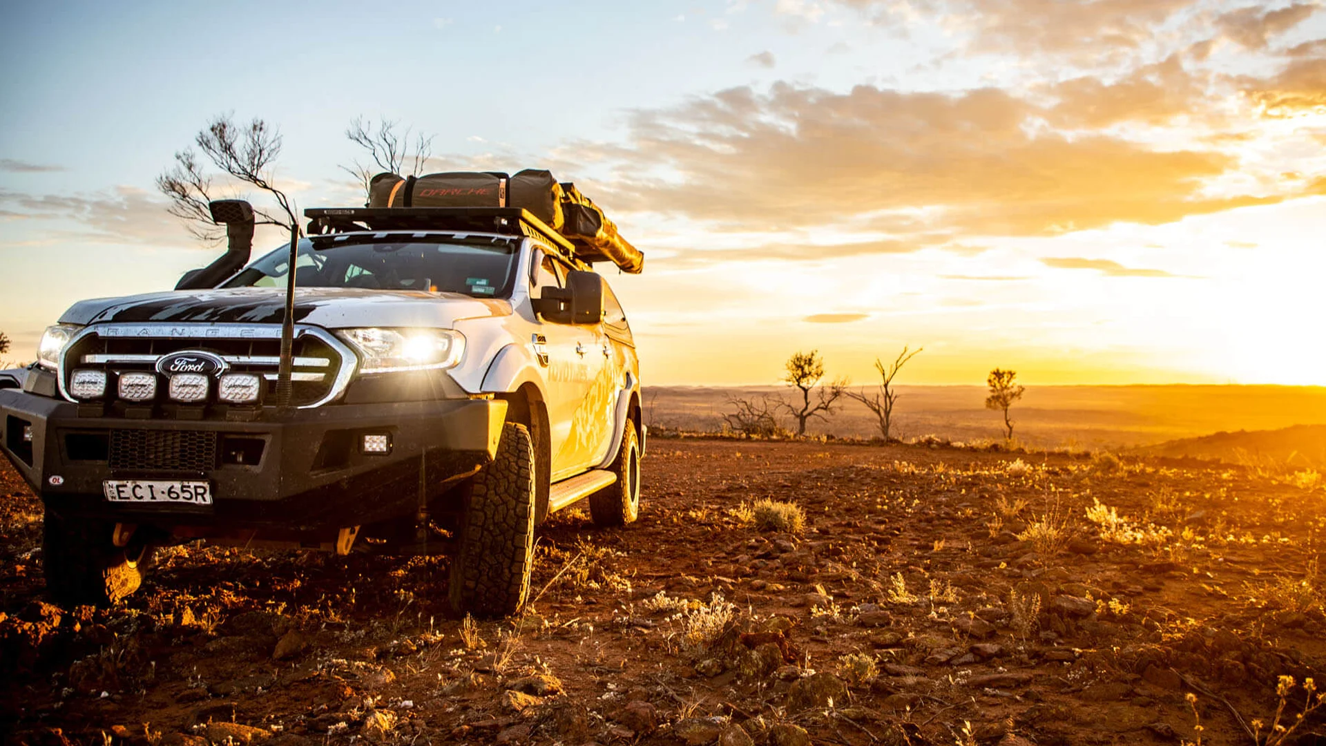 4WD on all-terrain tyres in the outback at sunset Dual-cab touring 4WD with roof rack, snorkel and driving lights on red outback dirt at sunset