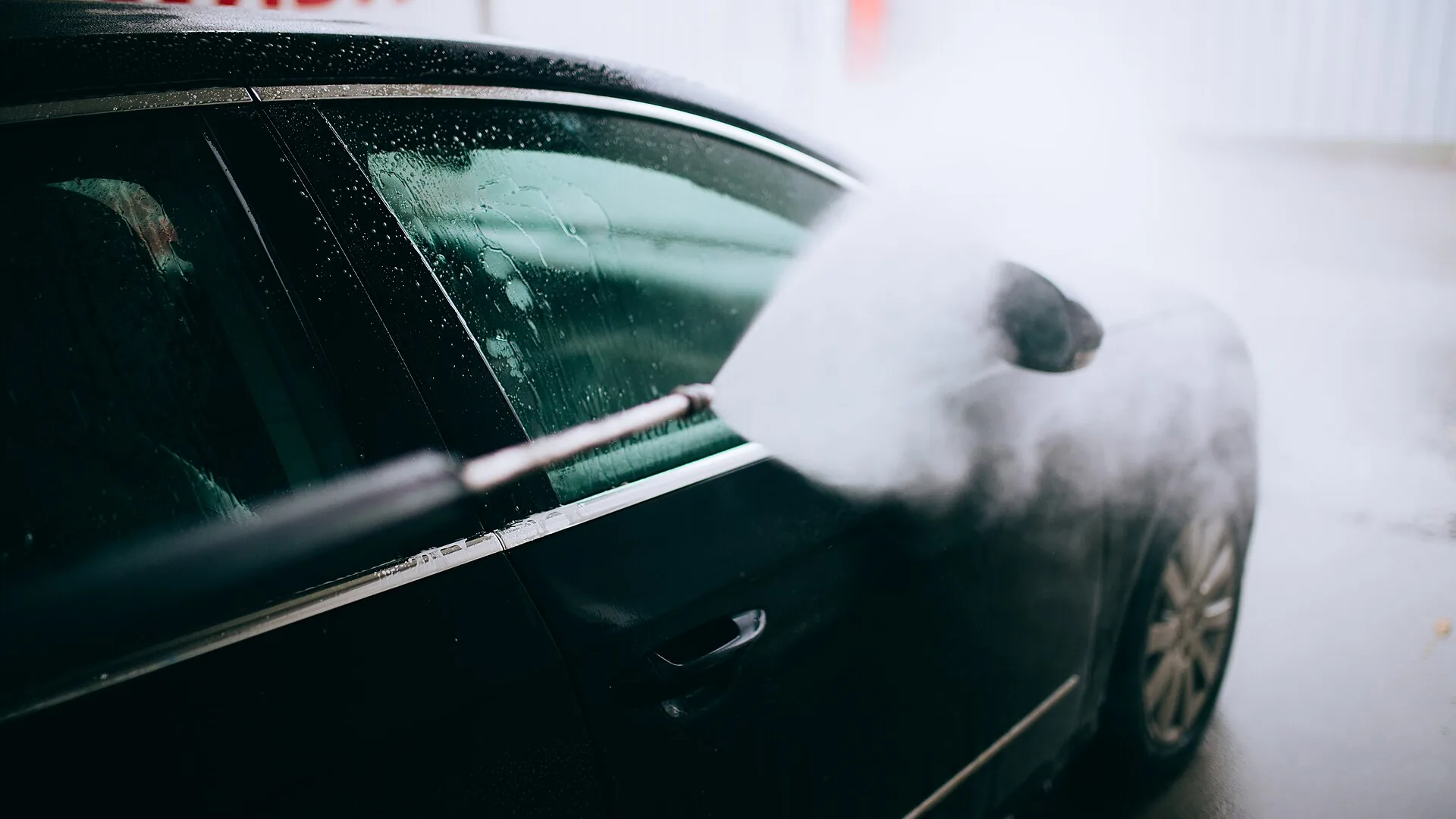 Pressure washing a car Pressure washer lance spraying a fan of water across the side window and door of a dark Volkswagen Passat